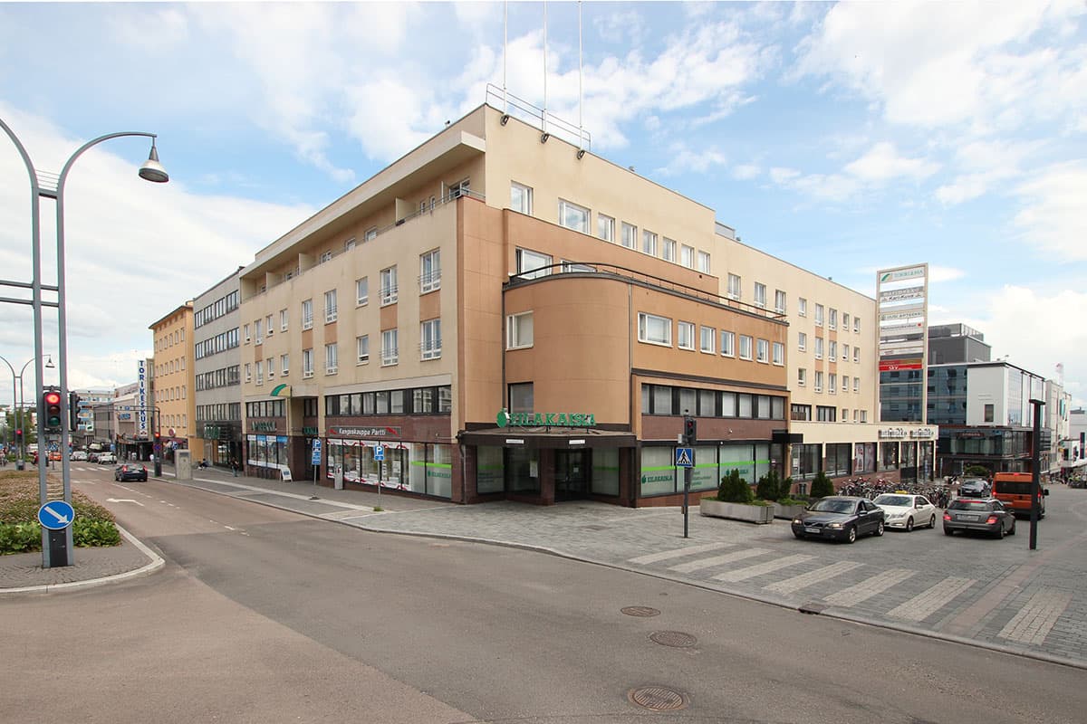 Monikerroksinen rakennus kaupungin kadun kulmassa ja katunäkymä, jossa on autoja.