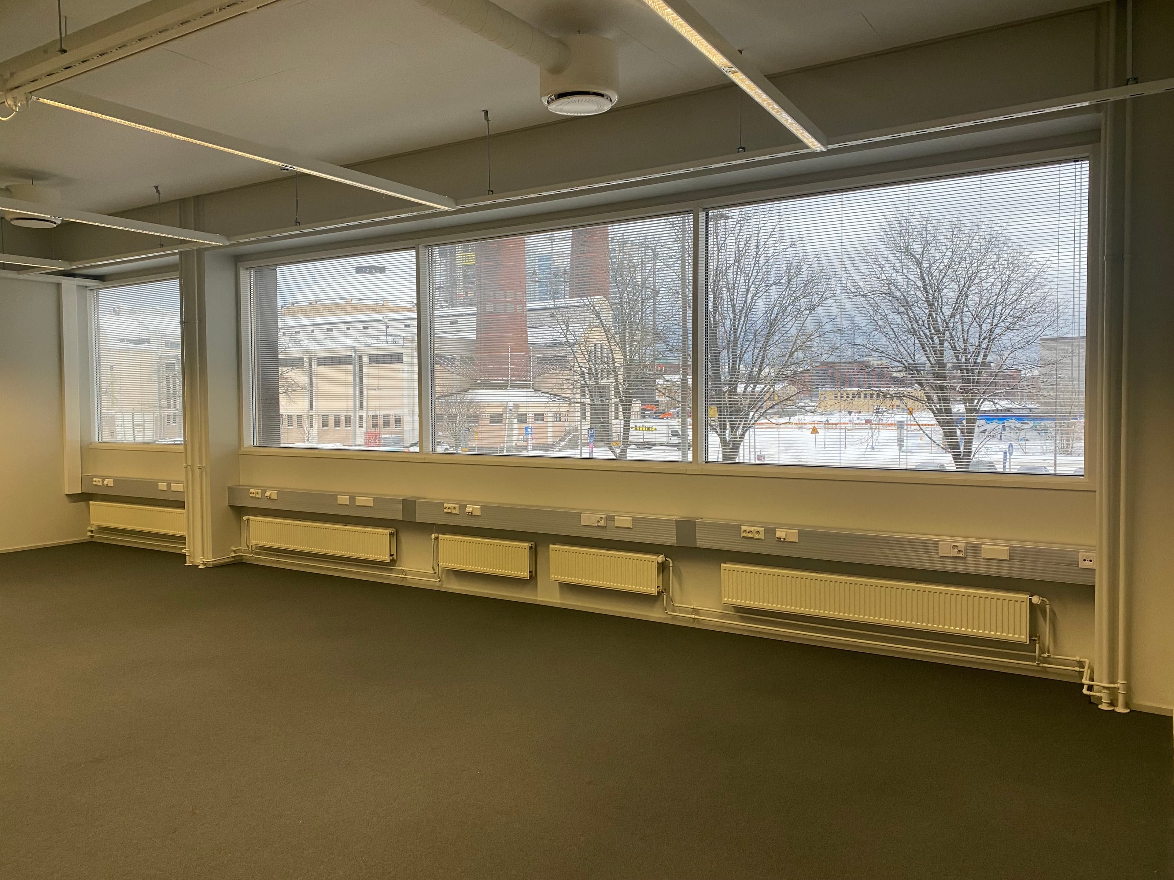 Tyhjä valoisa toimistotila, jossa on suuret ikkunat ja näkymä ulos.