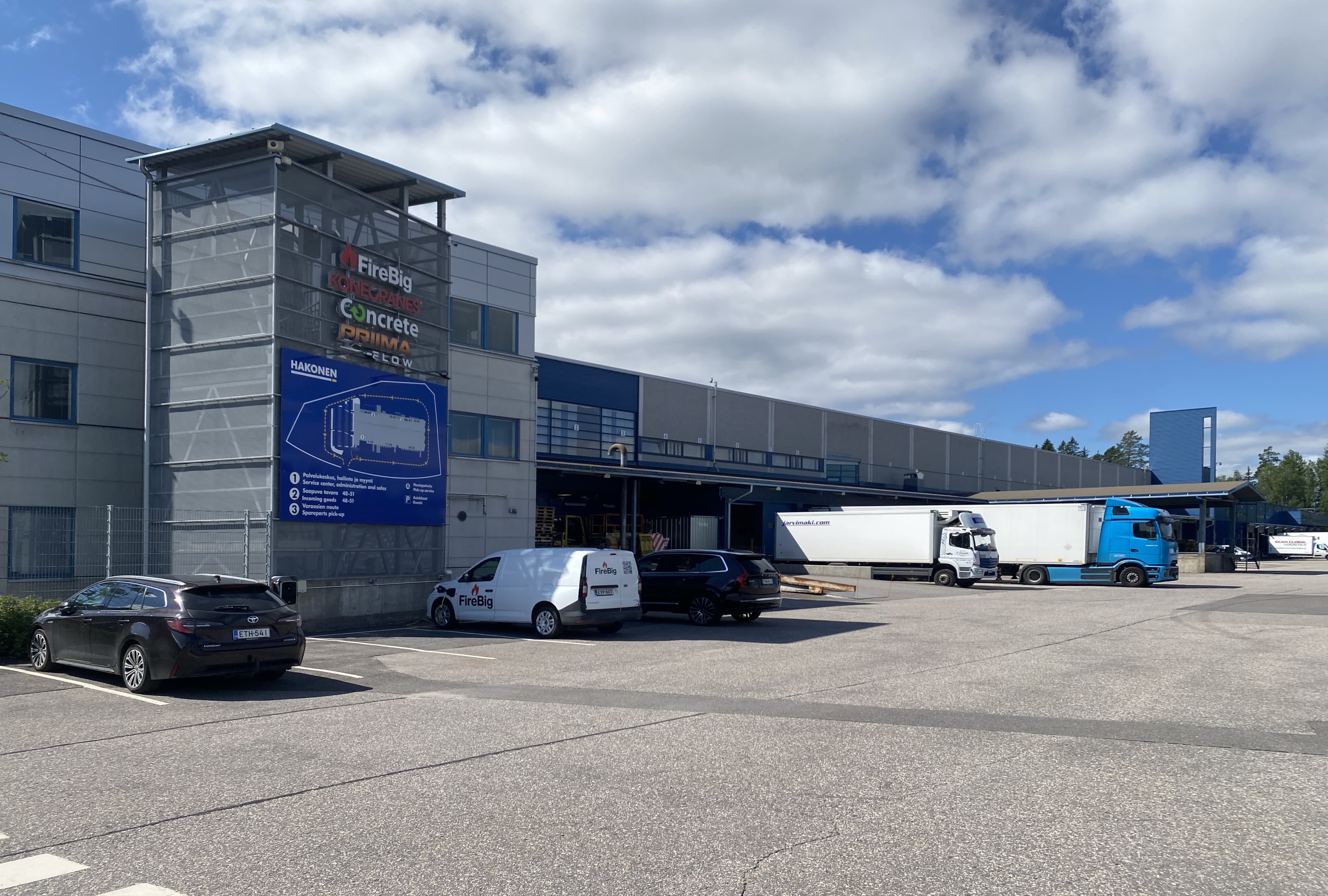 Teollisuusrakennus ja logistiikkakeskus, jonka pihalla on pysäköityjä autoja ja kuorma-autoja.