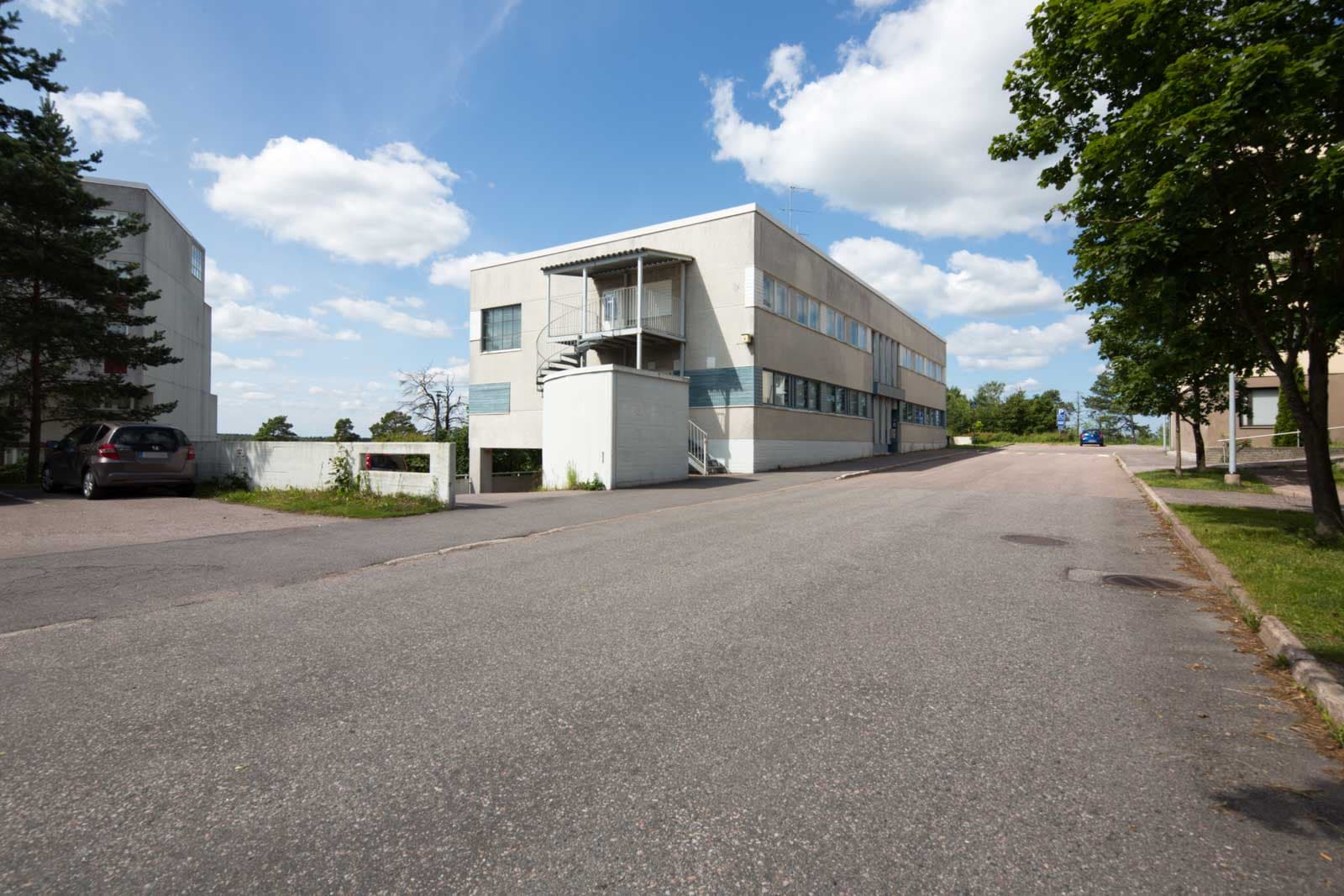 Vaalea kaksikerroksinen rakennus asfalttitien varrella aurinkoisena päivänä.