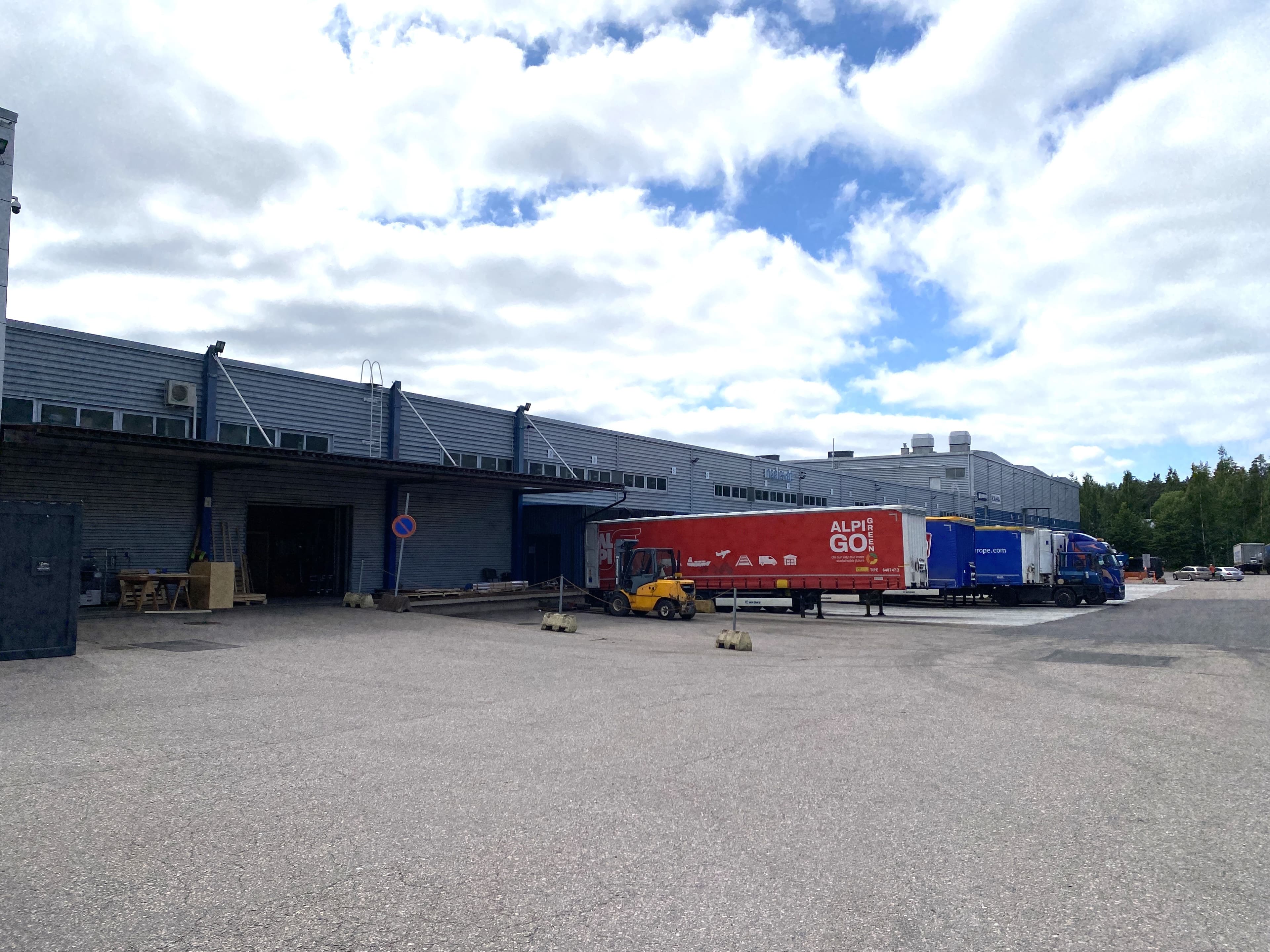 Logistiikkakeskuksen lastausalue, jossa on kuorma-autoja ja trukki.
