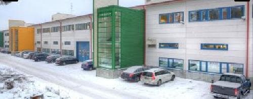 Teollisuusrakennus ja pysäköityjä autoja lumisessa maisemassa.