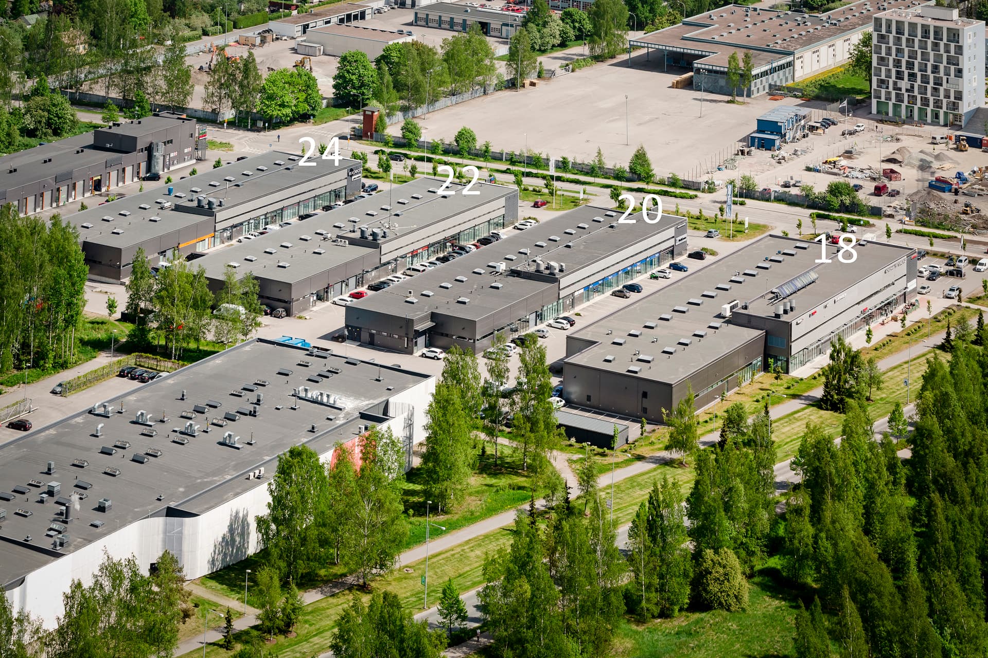 Ilmakuva teollisuus- ja liikealueesta, jossa on useita numeroituja rakennuksia ja ympäröivää kasvillisuutta.