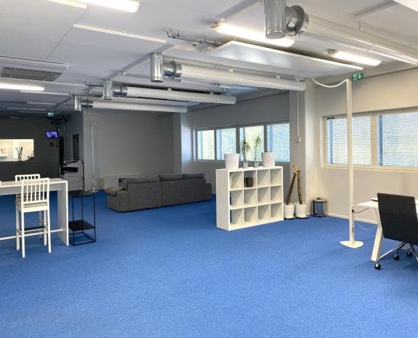 Valoisa ja avara toimistotila, jossa on sininen kokolattiamatto, harmaa sohva ja valkoisia kalusteita.