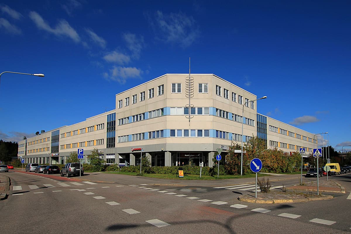 Monikerroksinen liikerakennus kadunristeyksessä aurinkoisena päivänä.