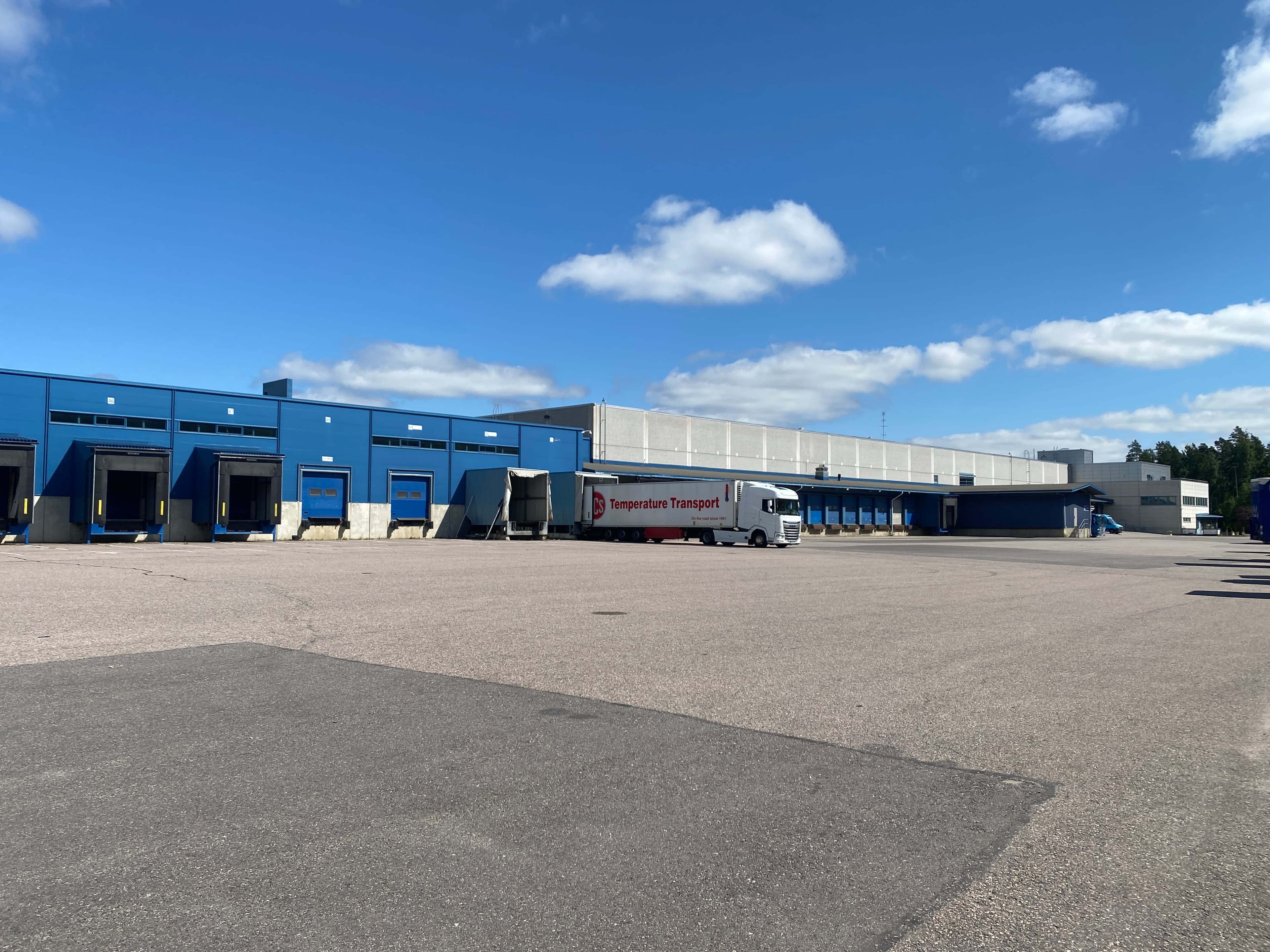 Sininen teollisuusrakennus ja lastauslaiturilla oleva kuorma-auto aurinkoisena päivänä.