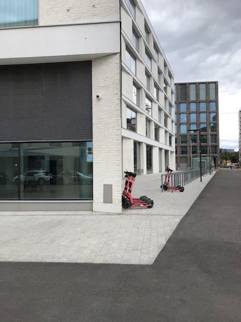 Punaisia sähköpotkulautoja pysäköitynä modernin valkoisen rakennuksen eteen kaupunkiympäristössä.