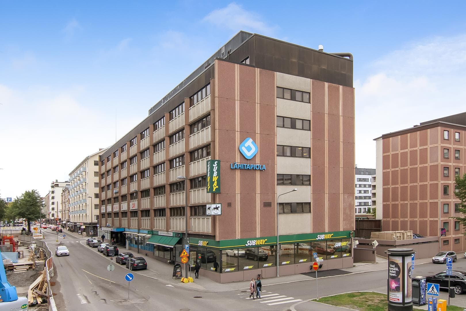 Monikerroksinen liikerakennus kadun kulmassa kaupunkiympäristössä.