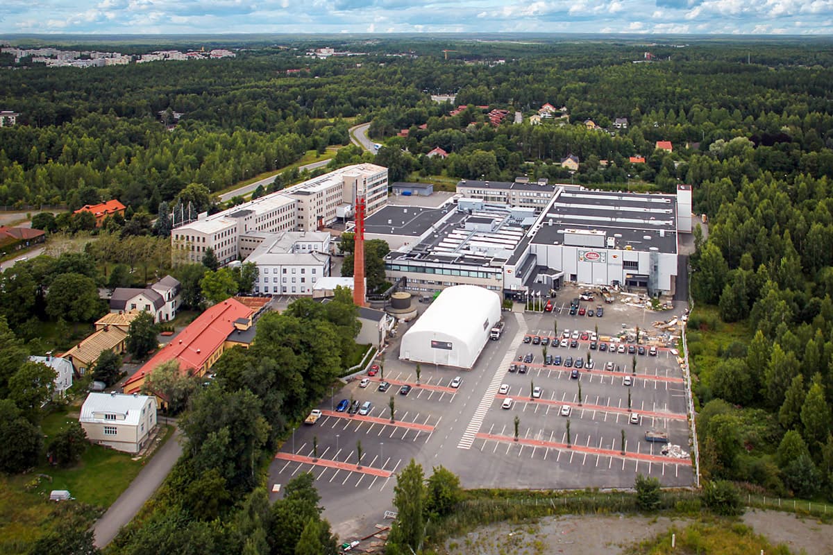 Ilmakuva metsän ympäröimästä teollisuusalueesta ja sen pysäköintialueesta.
