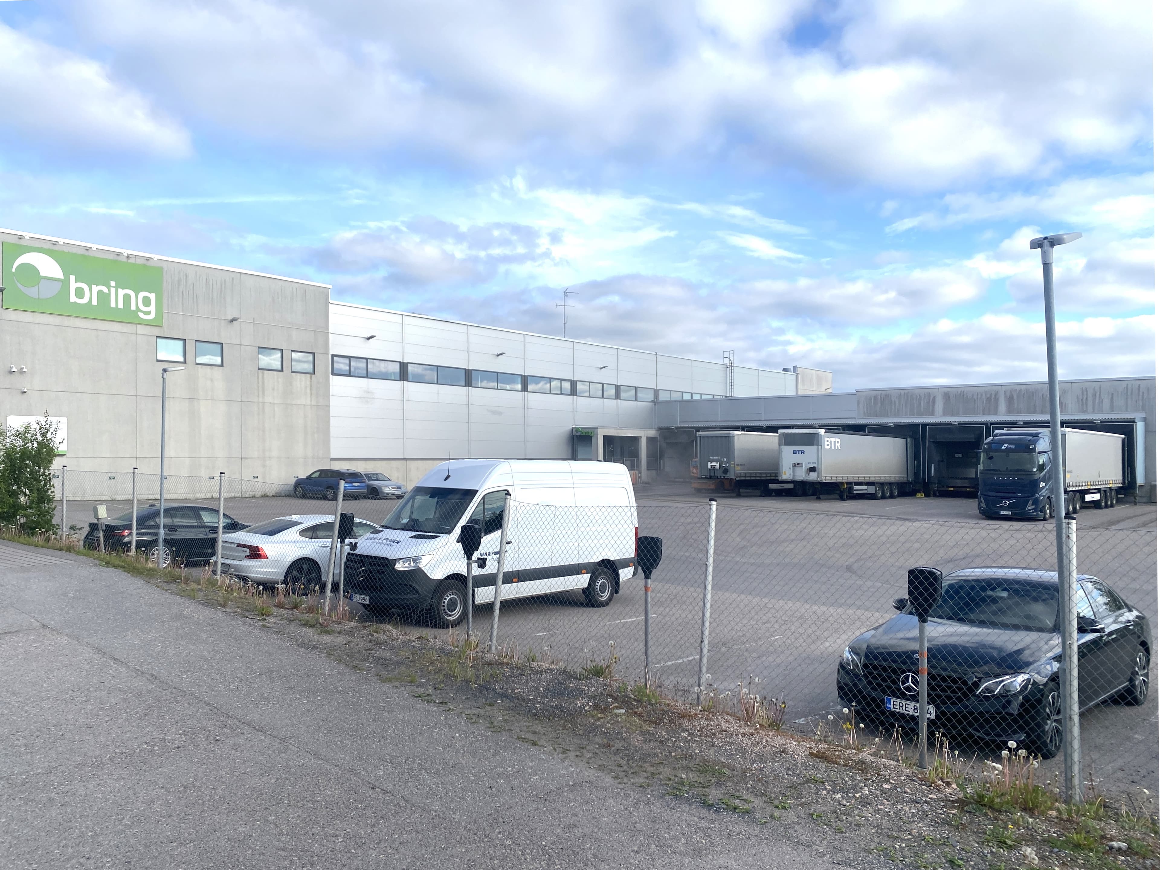 Logistiikkakeskuksen piha, jossa on pysäköityjä autoja ja rekkoja lastauslaitureilla.