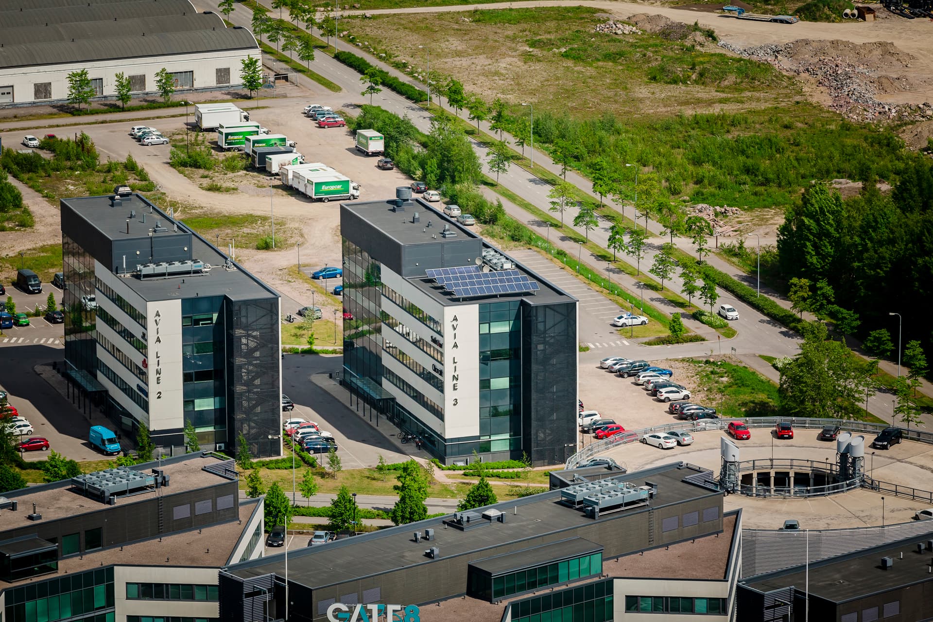 Ilmakuva modernista yritysalueesta ja toimistorakennuksista parkkipaikkoineen.