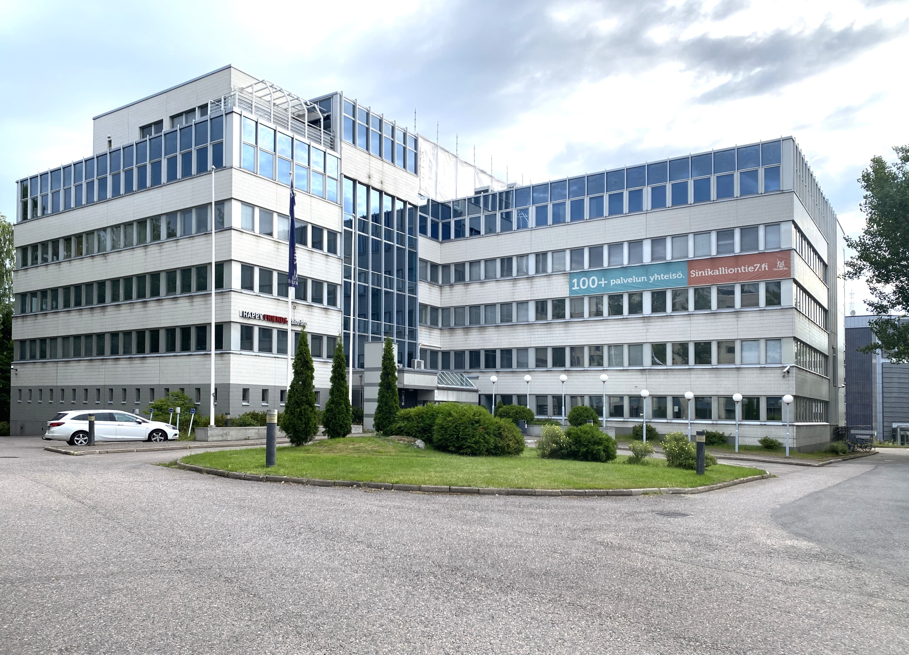 Vaalea monikerroksinen toimistorakennus ja sen edustalla oleva piha-alue.