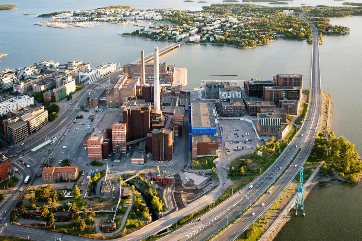 Ilmakuva rannikkokaupungin teollisuus- ja toimistoalueesta, jossa näkyy suuri voimalaitos, valtatie ja merellinen maisema saarineen.