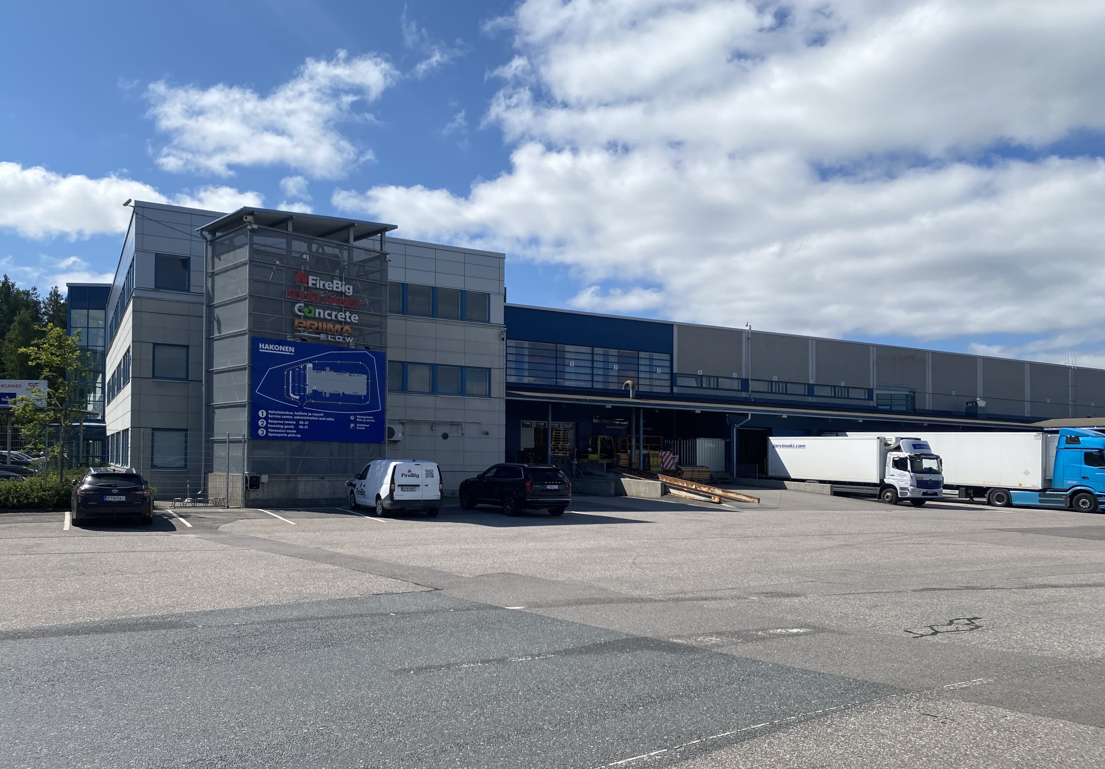 Teollisuusrakennus ja logistiikkakeskus, jonka pihalla on pysäköityjä autoja ja kuorma-autoja.