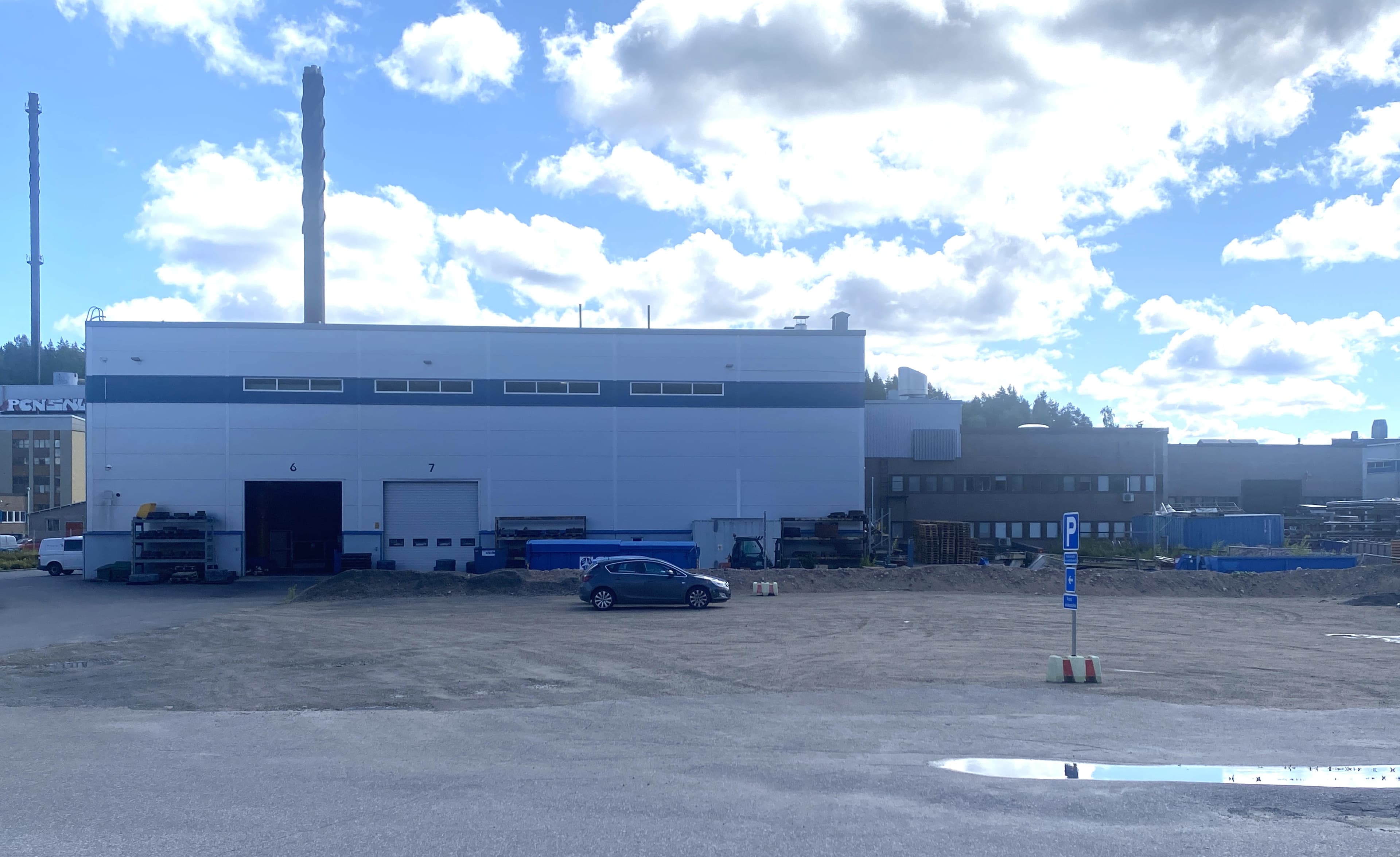 Teollisuusrakennus ja sen pihalla pysäköity auto aurinkoisena päivänä.