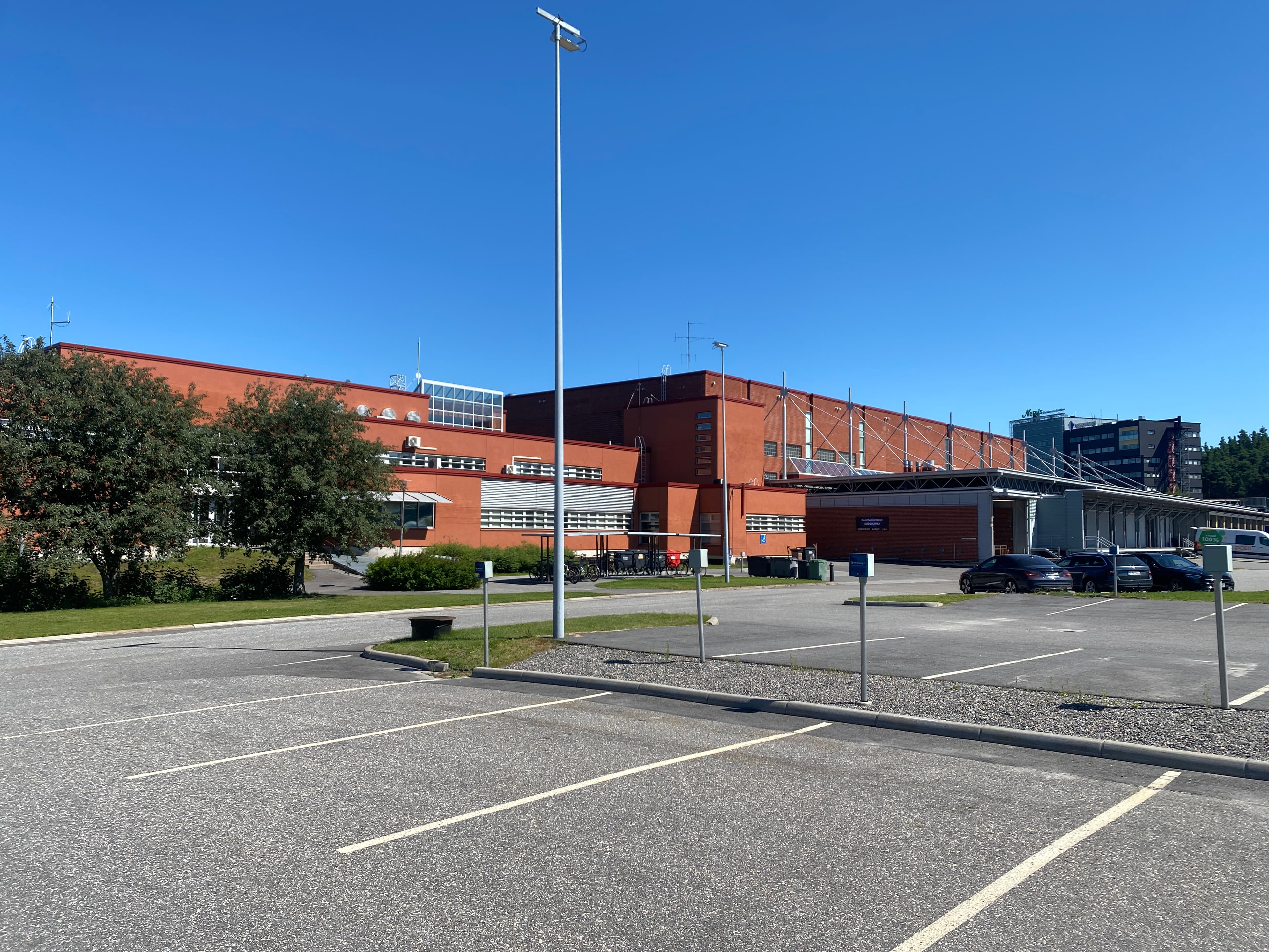 Tyhjä parkkipaikka suuren punaisen rakennuksen edessä aurinkoisena päivänä.