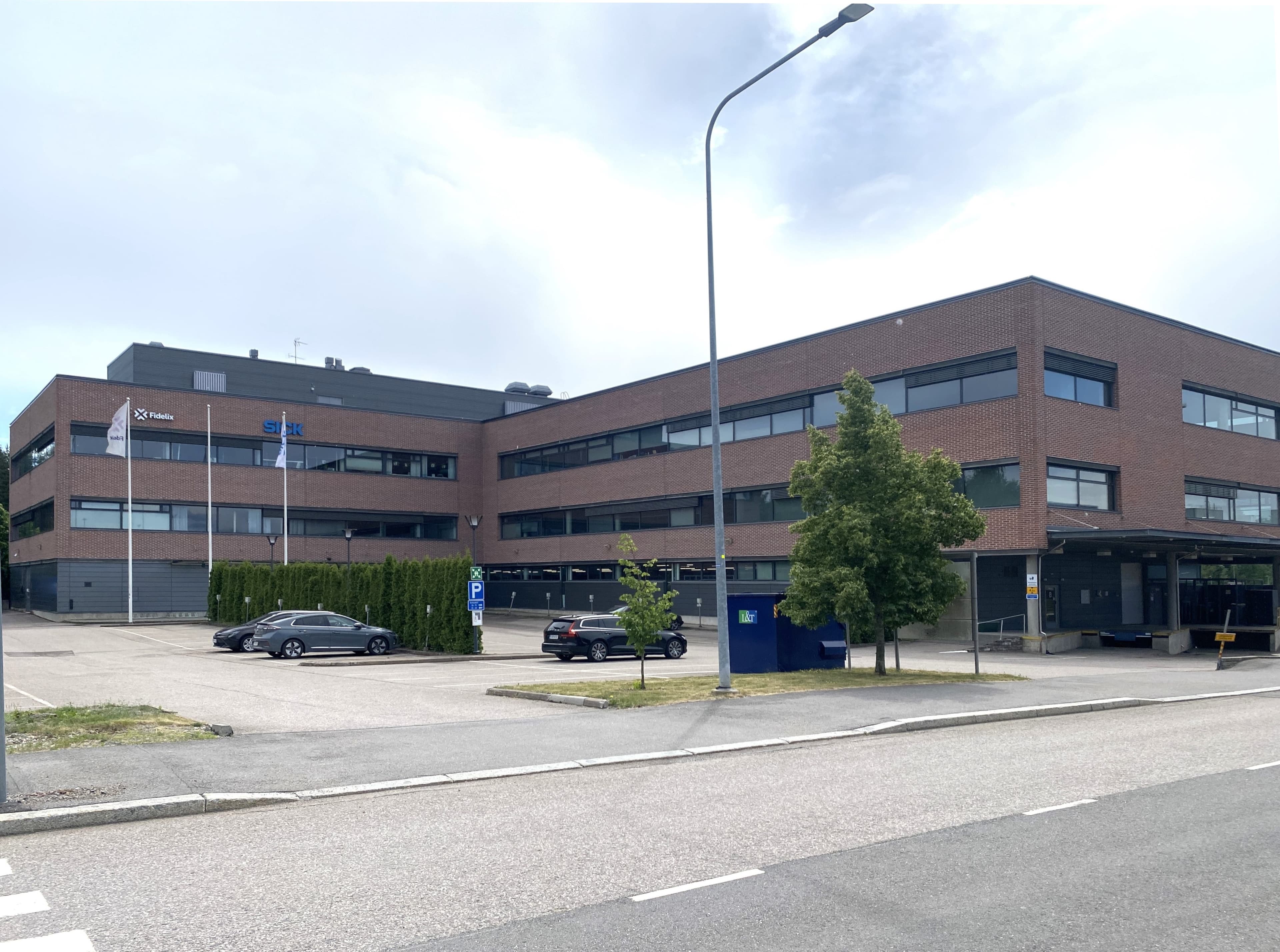 Kolmikerroksinen punatiilinen toimistorakennus ja sen edustalla oleva pysäköintialue.