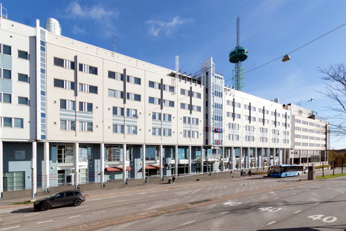 Valkoinen liikerakennus ja katu, jonka taustalla näkyy korkea radiotorni.