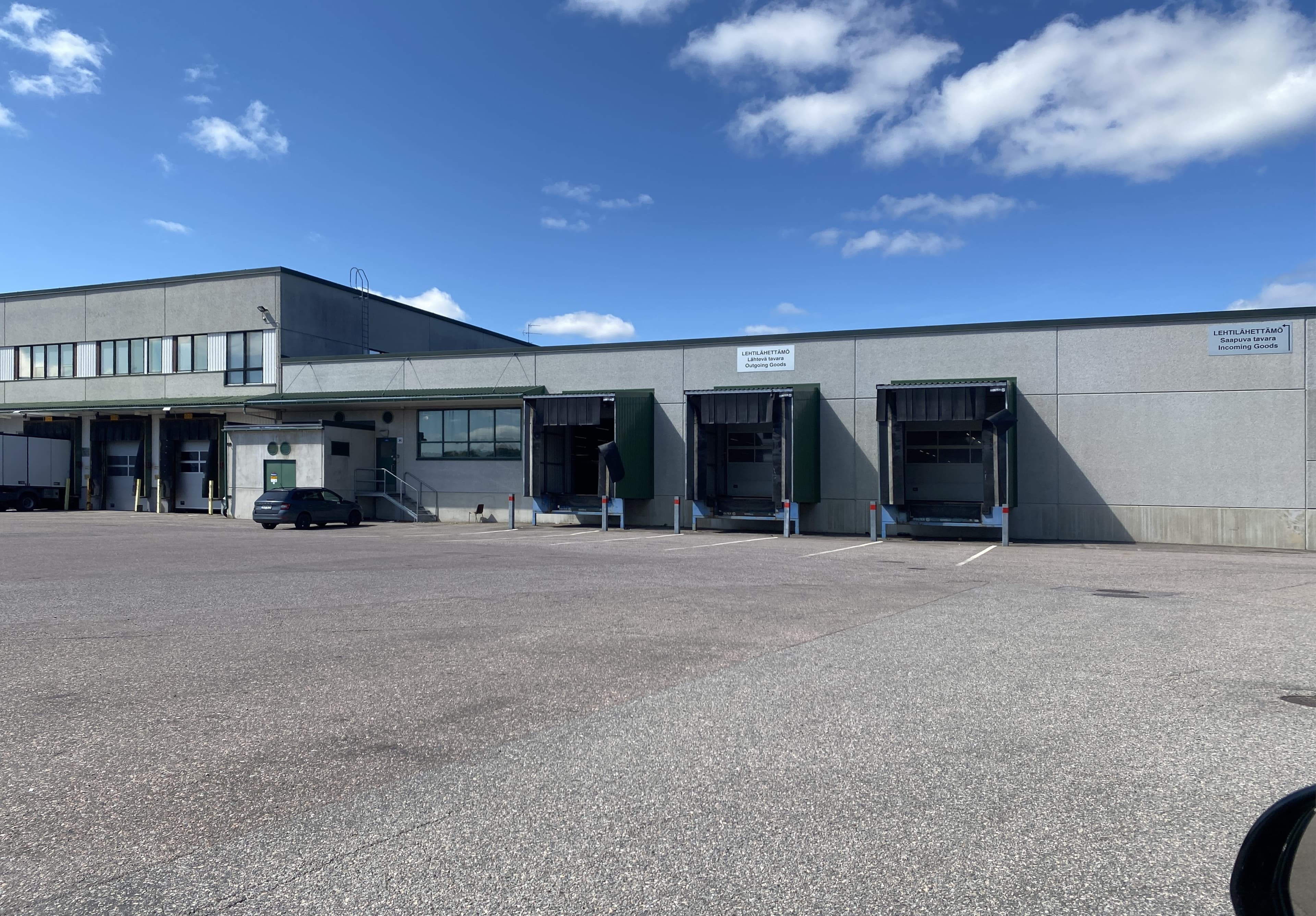 Harmaa teollisuusrakennus, jossa on useita lastauslaitureita asfaltoidun piha-alueen laidalla.