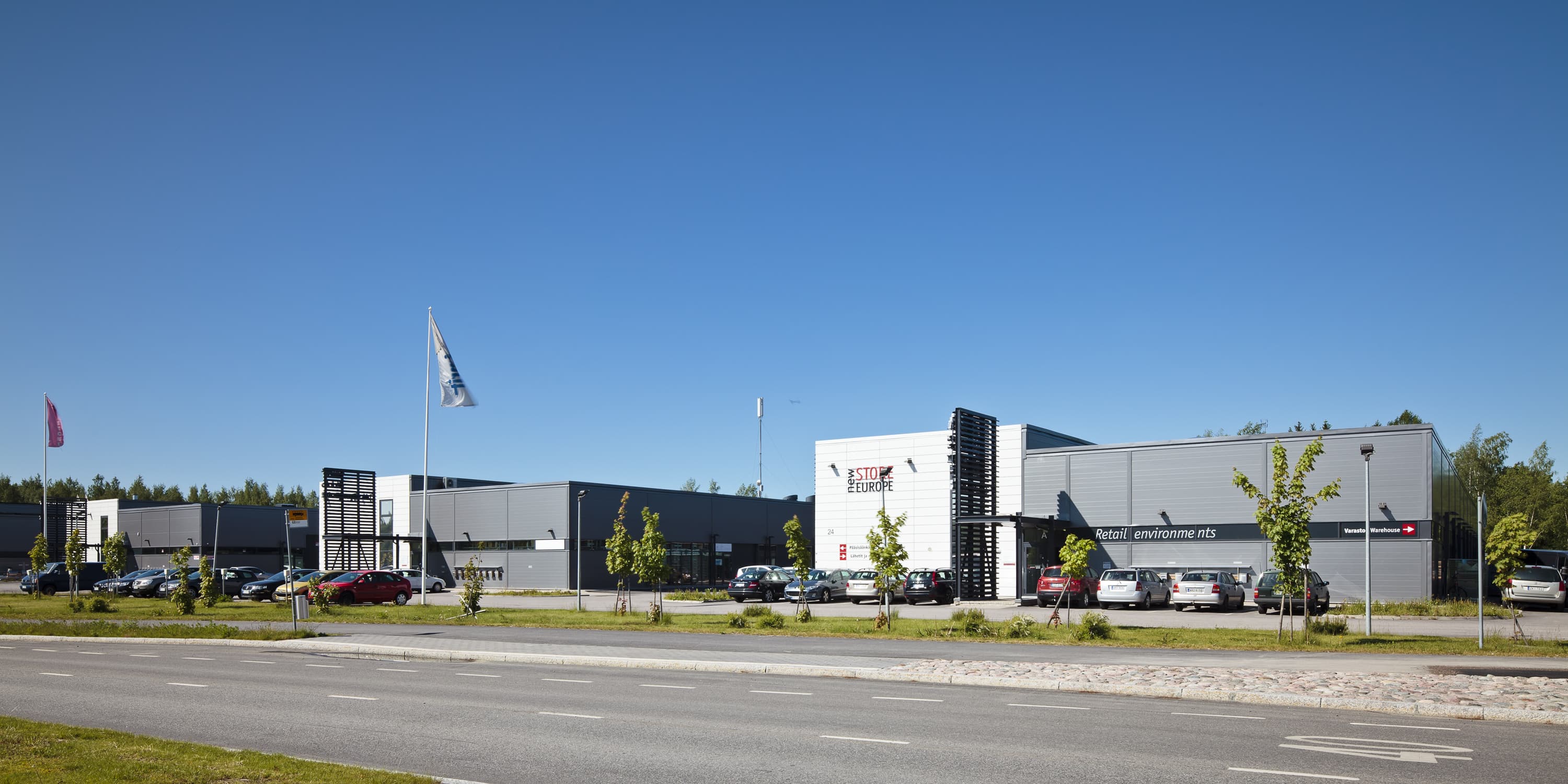 Näkymä modernista liikerakennuksesta ja sen parkkipaikasta aurinkoisena päivänä.