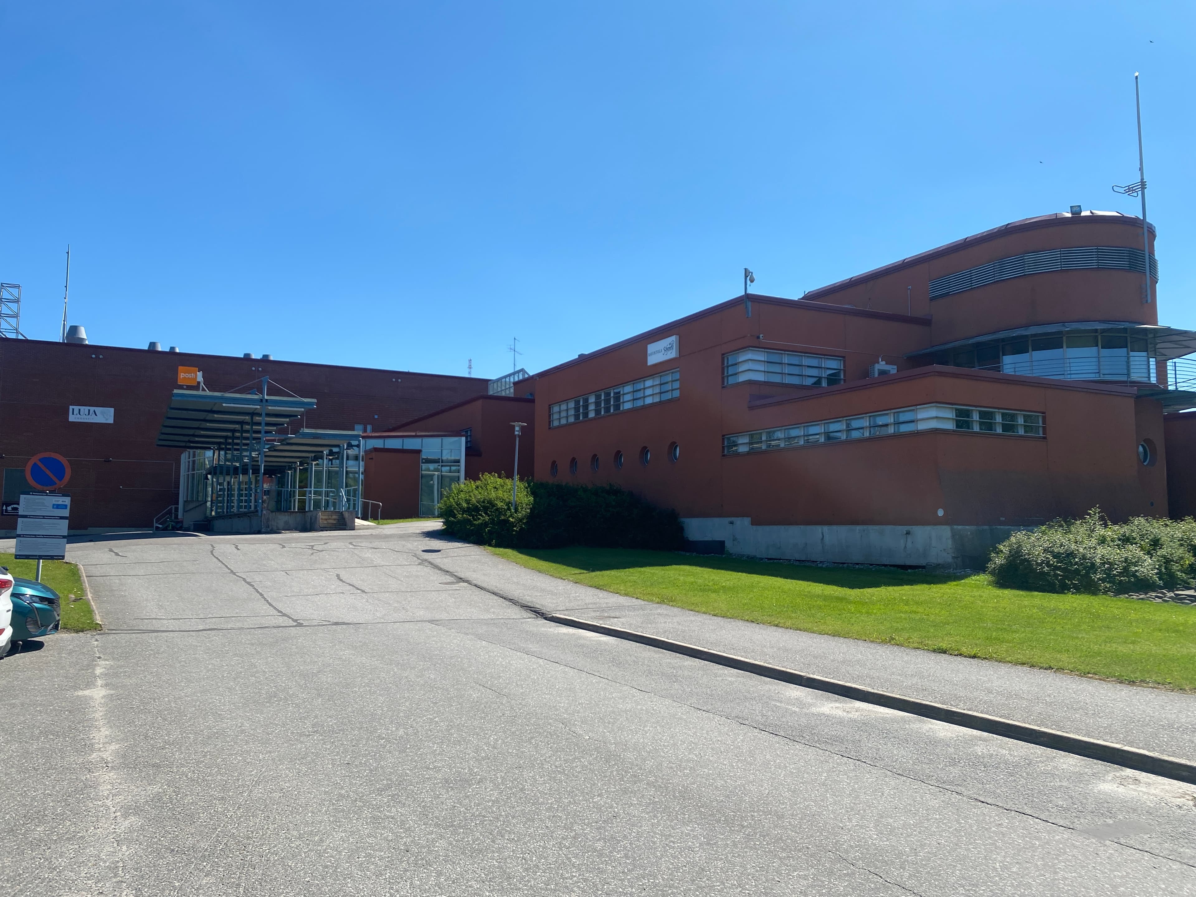 Punainen liikerakennus ja asfaltoitu piha-alue aurinkoisena päivänä.
