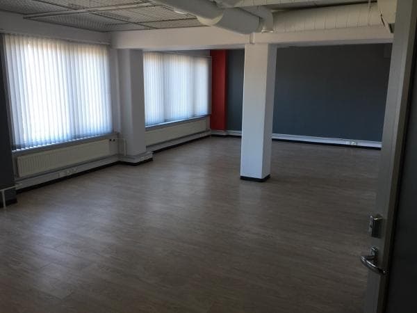 Tyhjä ja valoisa toimistotila, jossa on vaalea lattia ja suuret ikkunat.