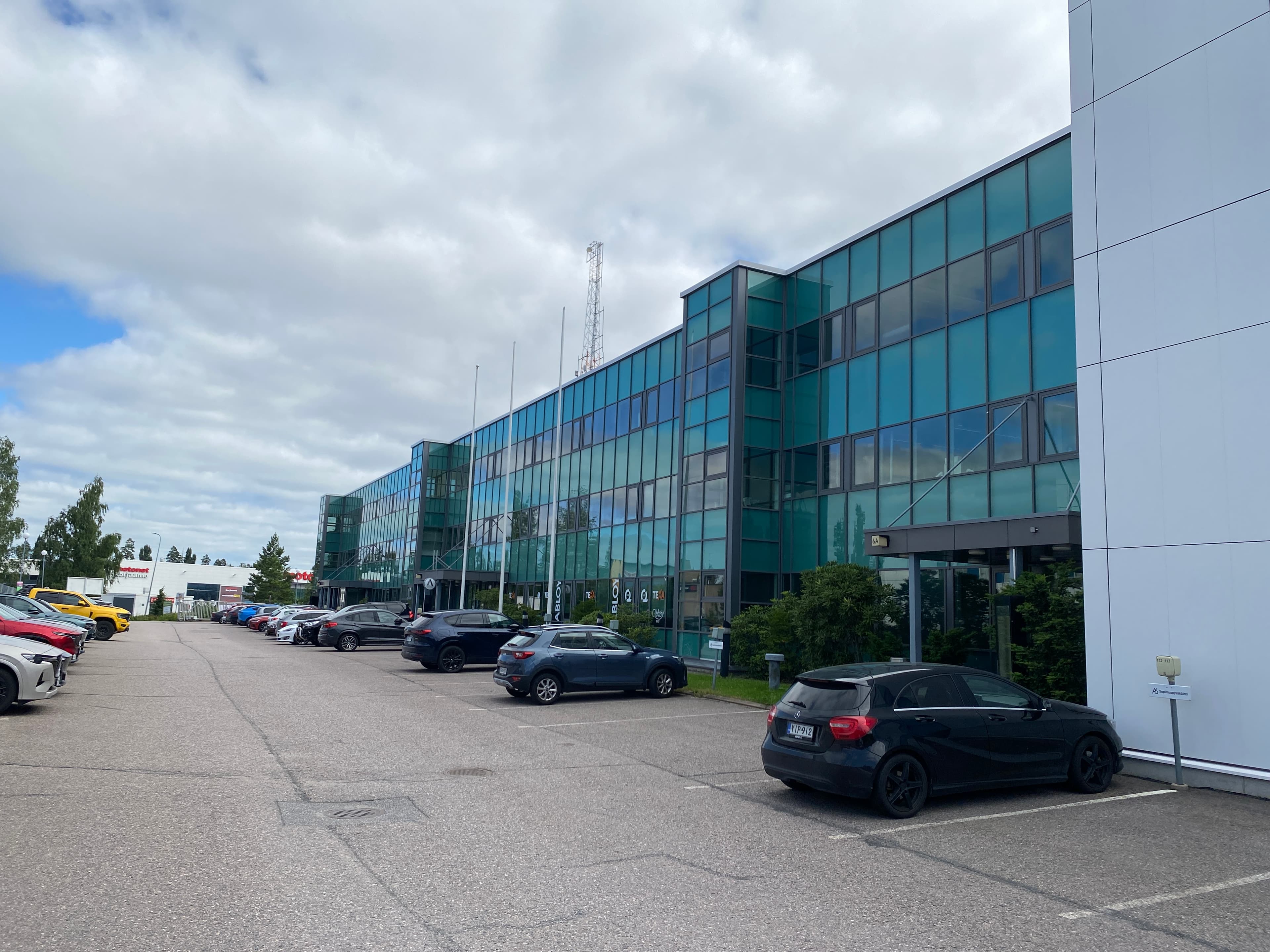 Moderni lasijulkisivuinen toimistorakennus ja sen edustalla oleva parkkipaikka.