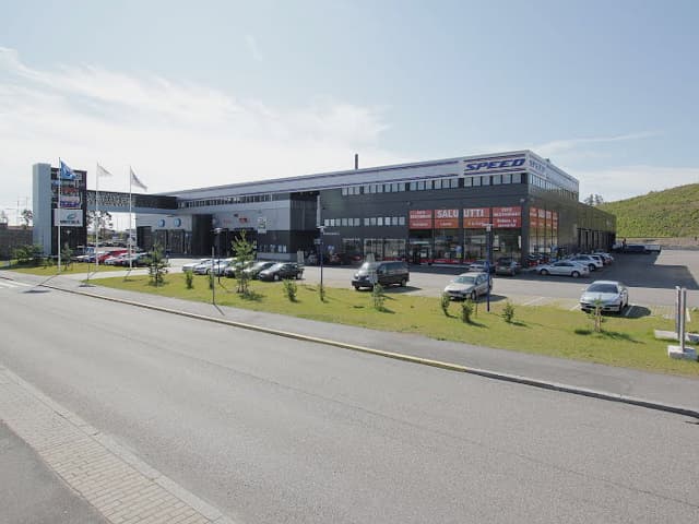Suuri liikerakennus ja sen edessä oleva pysäköintialue autoineen aurinkoisena päivänä.