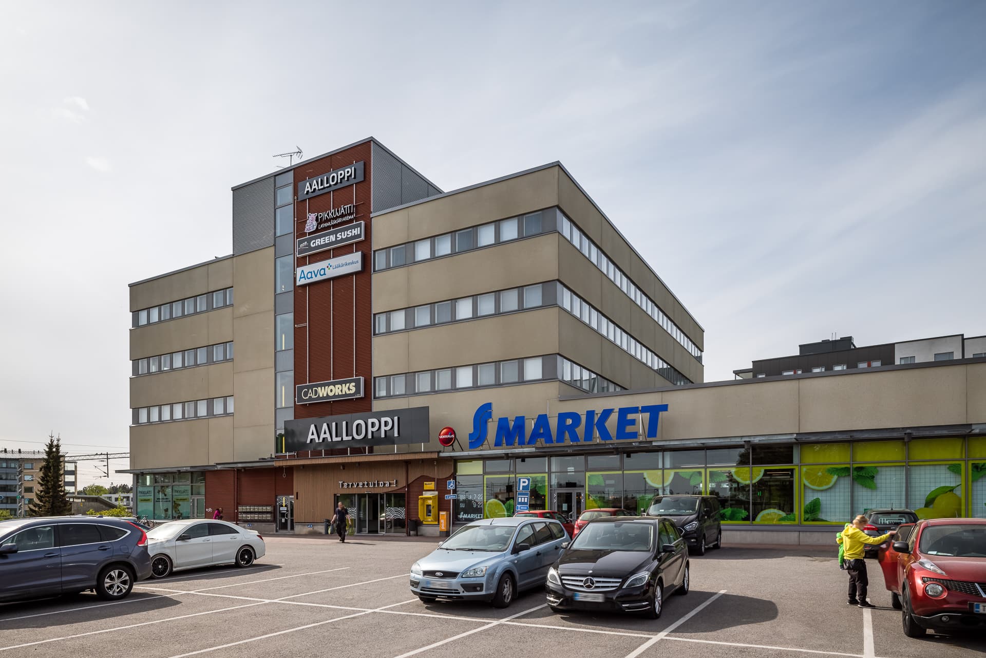Liikerakennus ja sen edessä oleva pysäköintialue autoineen.