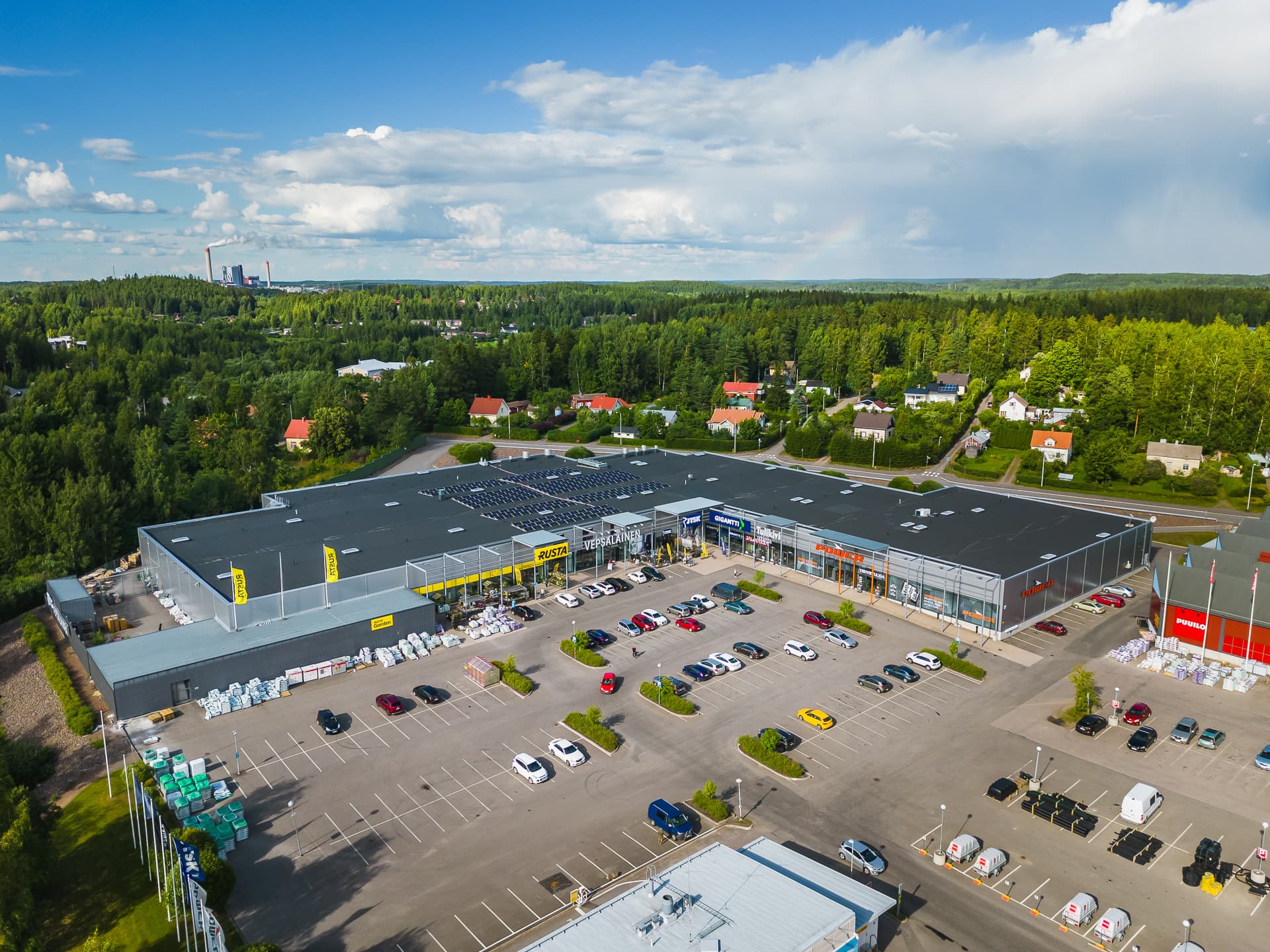 Ilmakuva liikekeskuksesta ja sen pysäköintialueesta metsäisessä maisemassa.
