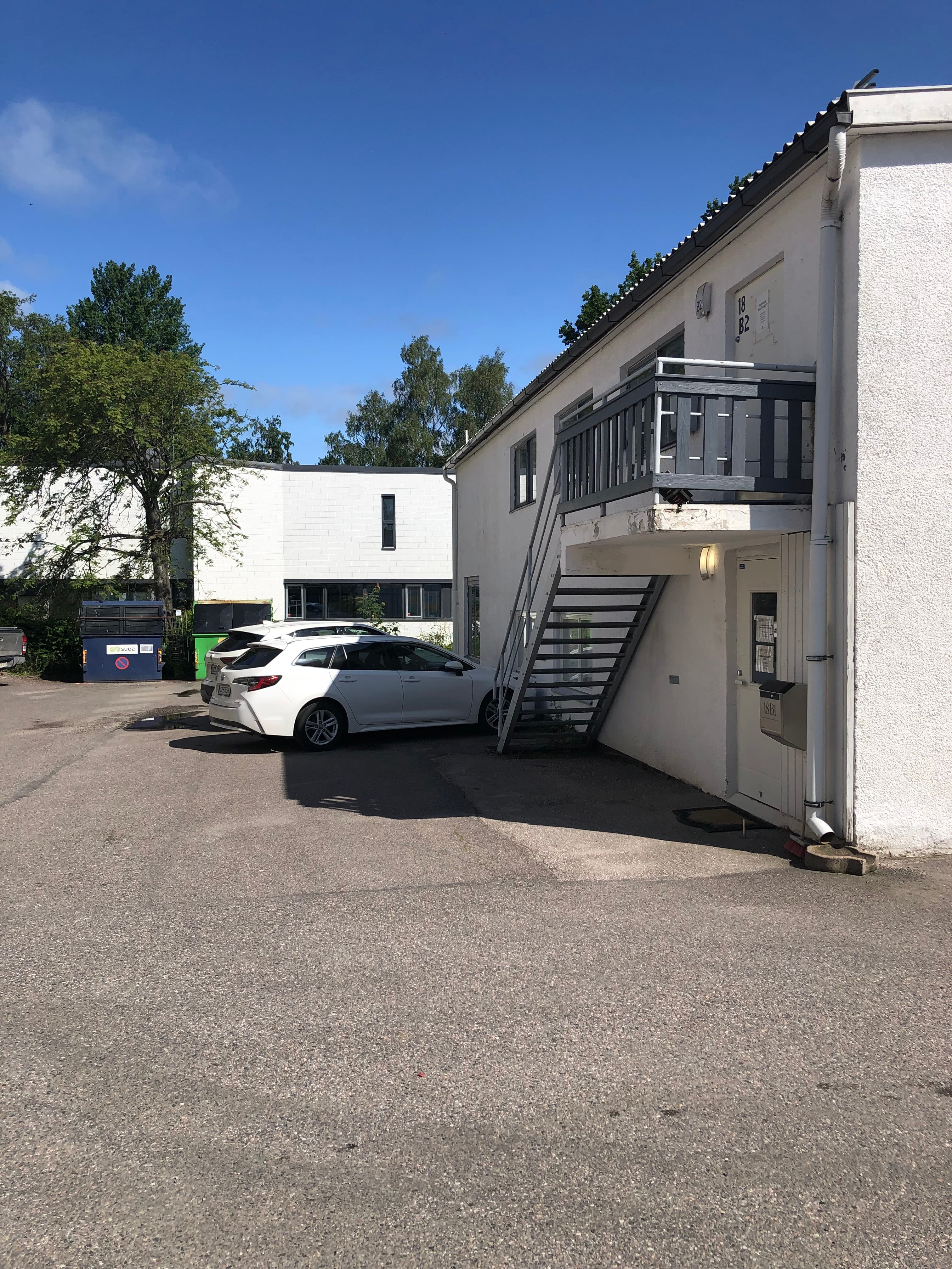 Valkoinen auto pysäköitynä valkoisen rakennuksen eteen, jossa on metalliset ulkoportaat.
