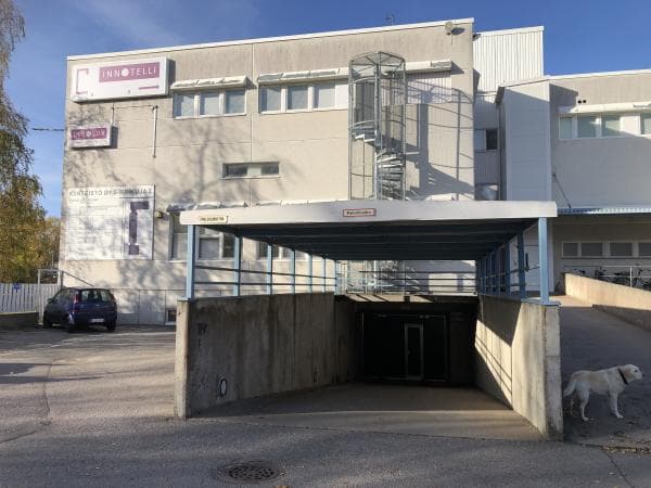 Innotelli-toimistorakennus, jonka edustalla on ramppi parkkihalliin, ulkoiset kierreportaat ja valkoinen koira.