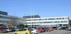 Valkoinen rakennus ja sen edustalla oleva täysi pysäköintialue aurinkoisena päivänä.