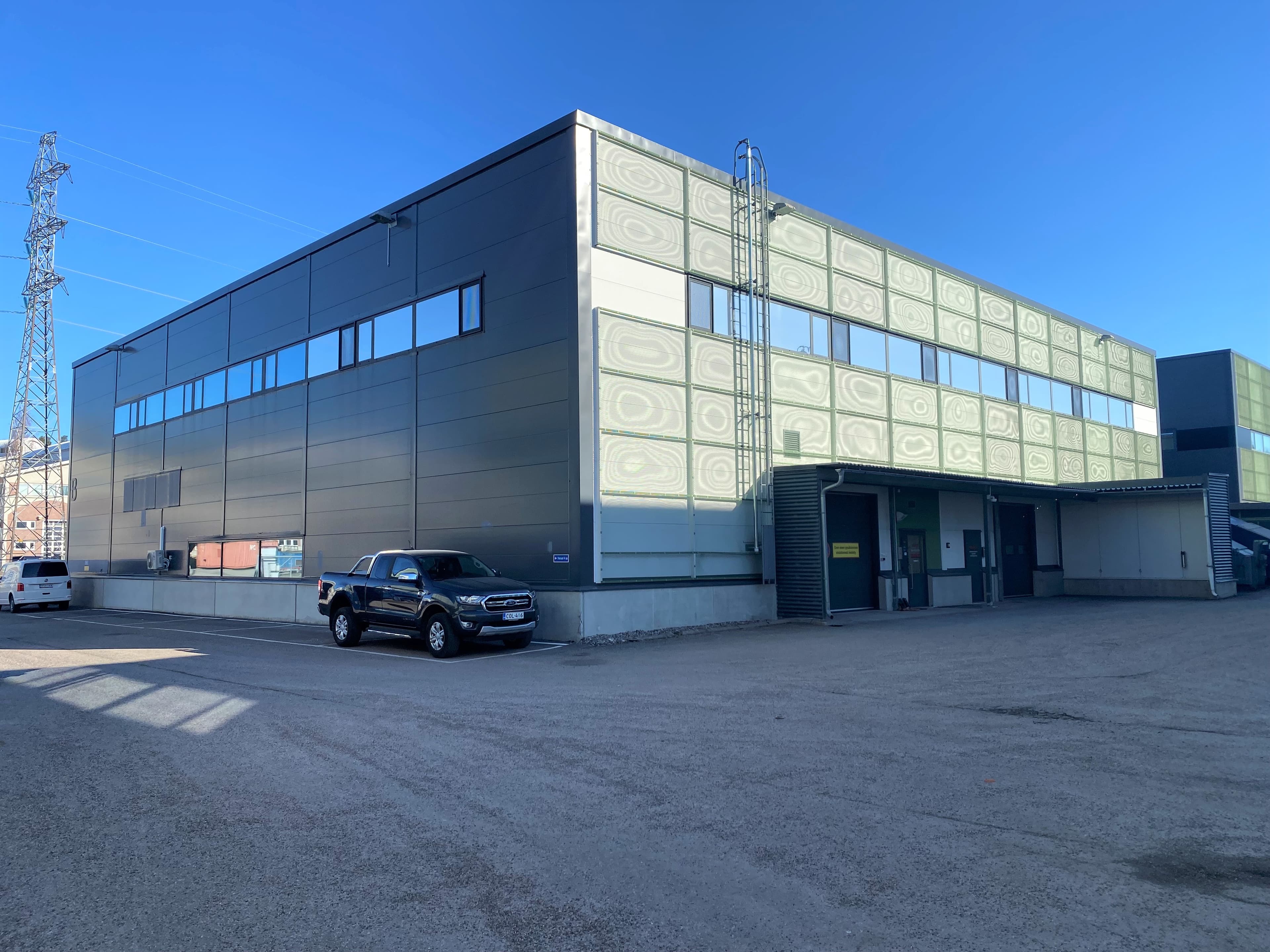 Moderni teollisuusrakennus ja sen edustalle pysäköity lava-auto.