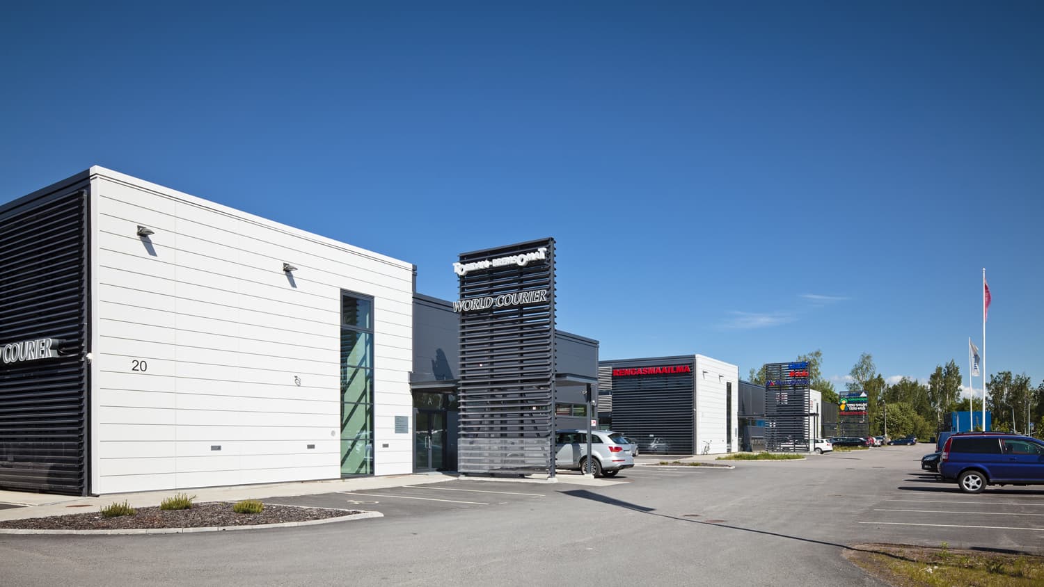 Moderni valkoinen liikerakennus ja pysäköintialue kirkkaana, aurinkoisena päivänä.
