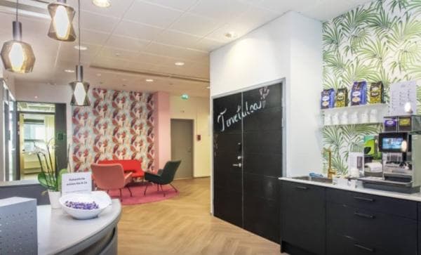 Värikäs ja valoisa toimiston aula, jossa on oleskelutila, vastaanottotiski ja kahvipiste.