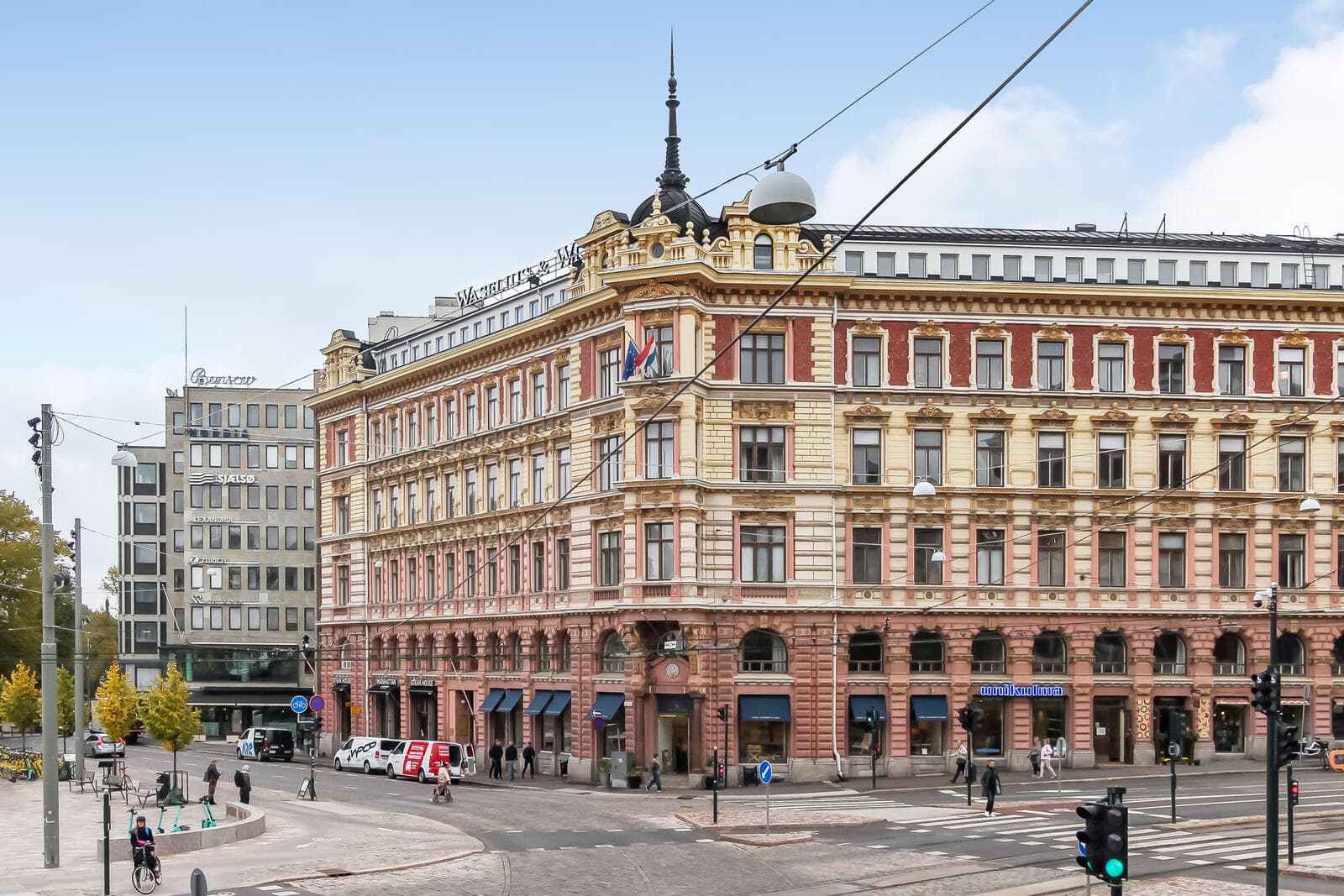 Suuri historiallinen kulmarakennus vilkkaan kaupunkiristeyksen laidalla.