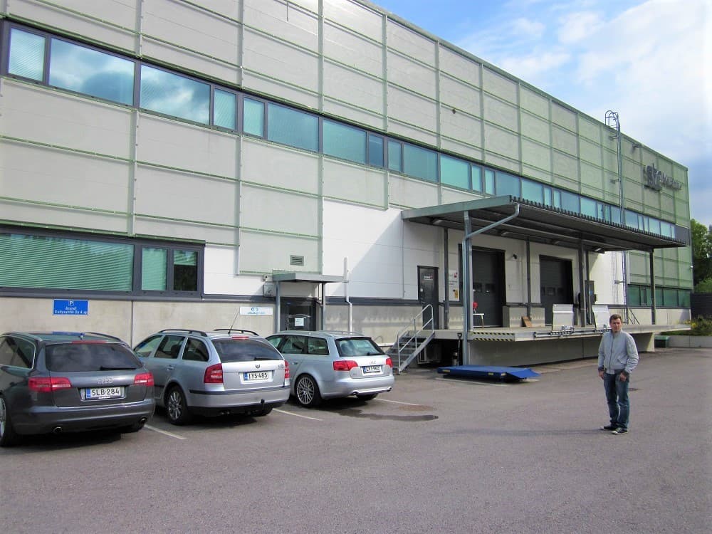 Toimistorakennuksen julkisivu, jonka edessä on pysäköityjä autoja ja lastauslaituri.