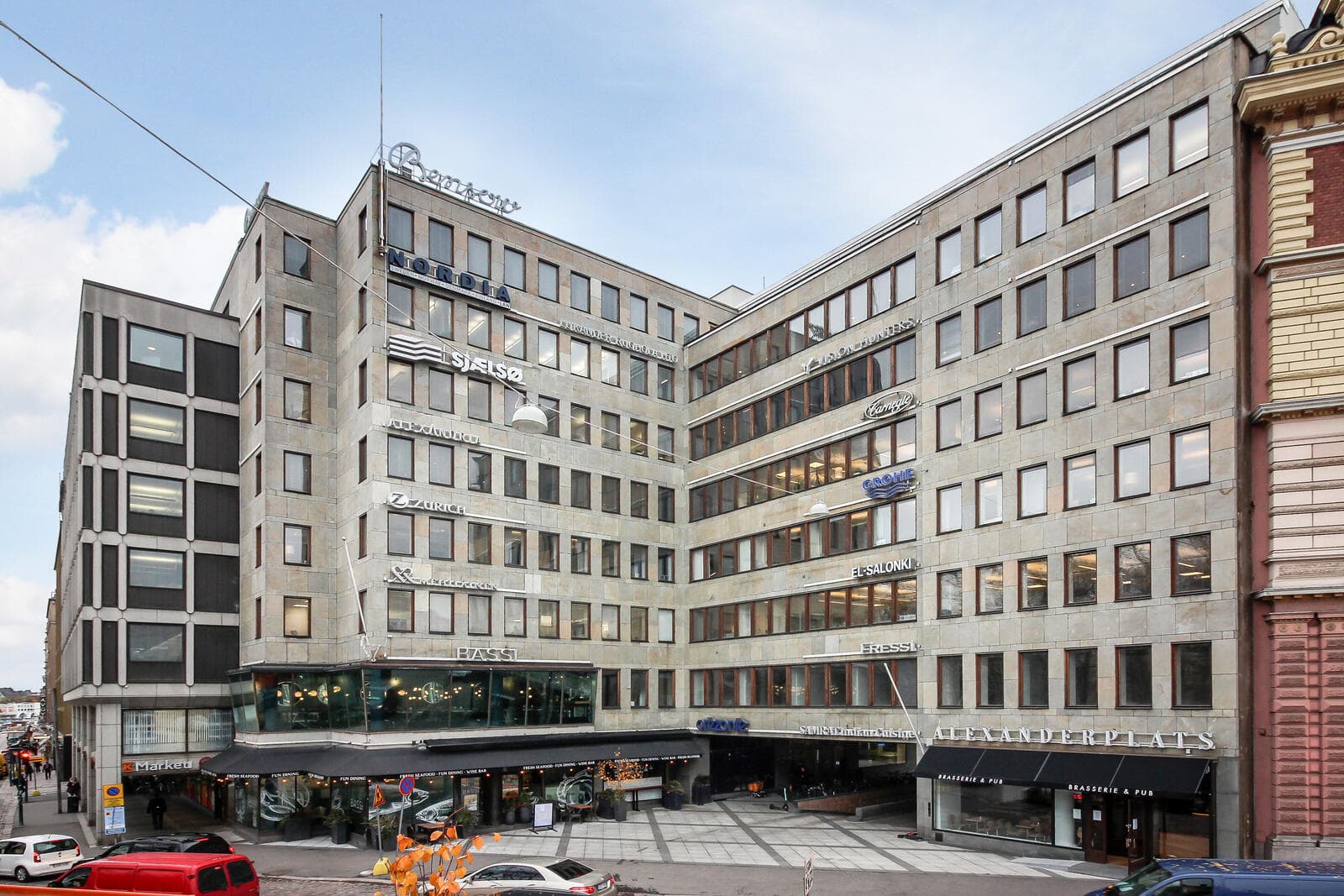 Monikerroksinen toimisto- ja liikerakennus, jonka julkisivussa on useita yrityskylttejä ja katutasossa ravintoloita.